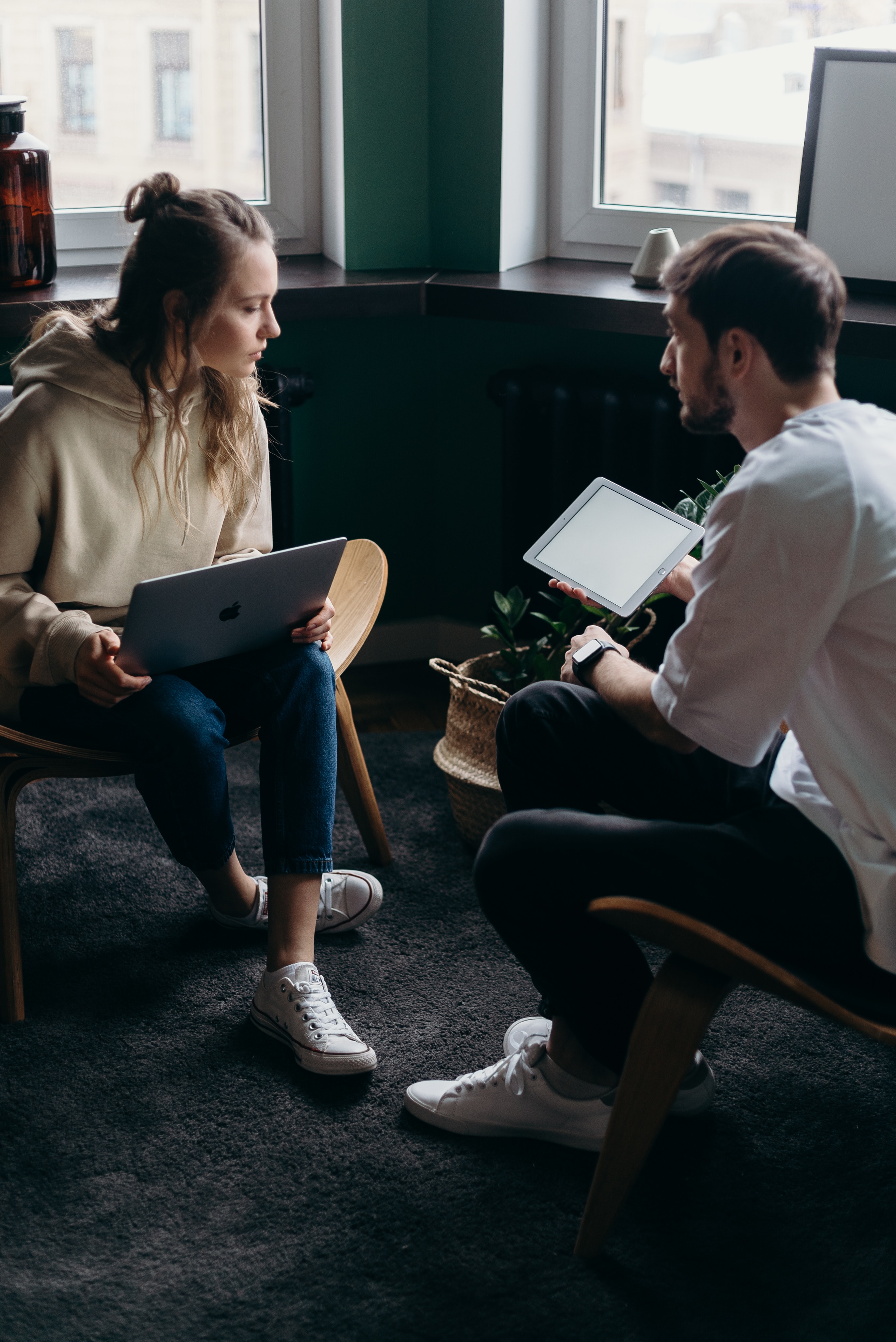 A woman holding a laptop and a man holding a tablet sitting indoor and talking about a planning a startup